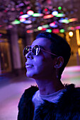 Young man in sunglasses looking up at neon lights