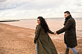 Happy couple in winter coats holding hands on beach