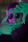 Young man in sunglasses forming finger frame in neon