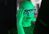 Woman with shaved head in neon glasses in green light