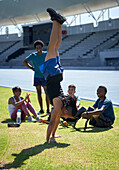 Athletes watching young man doing handstand in stadium