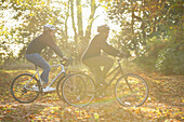 Couple bike riding through autumn leaves in sunny park