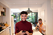 Happy confident young man using smart phone in kitchen