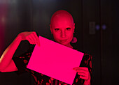 Woman with shaved head holding blank sign in red light