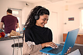 Happy woman with headphones working from home on laptop