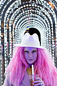Woman with pink hair in fedora under arch lights