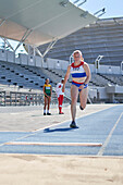 Female track and field athlete long jumping on sunny track
