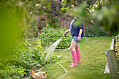 Woman with hose watering plants in summer vegetable garden