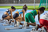 Female track and field athletes at starting blocks on track