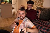 Happy gay male couple drinking wine and watching TV on sofa