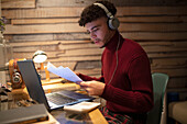 Young man with headphones and paperwork working late at home