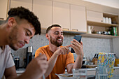 Happy gay male couple using smart phone and eating
