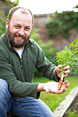 Happy man showing fresh harvested carrot in garden