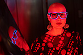 Woman with shaved head and neon glasses in red light