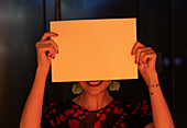 Smiling woman covering face with blank piece of paper