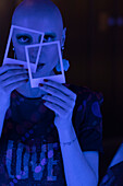 Woman with shaved head holding polaroids in blue light