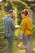 Couple with book and fresh harvested vegetables in garden