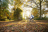 Carefree young woman riding bicycle through autumn leaves