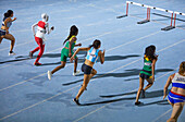 Female athletes running hurdle race on blue track