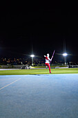 Female athlete throwing javelin in stadium at night