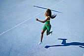 Female athlete throwing javelin on sunny blue track