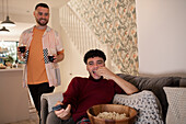 Happy gay couple with red wine and popcorn watching TV