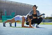 Trainer helping athlete doing planks on track