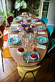 Oval dining table set with colourful plates, crystal glasses and bouquet of flowers