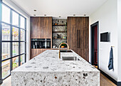 Stone kitchen island and cabinets with wooden fronts next to sliding glass element