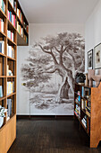 Floor-to-ceiling bookshelf and wallpaper with tree motif in the hallway