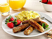 Turkey breakfast sausage links, scrambled eggs and fresh strawberries on a plate and orange juice