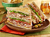 A double decker Turkey Breast, lettuce and tomato sandwich on a wooden plate