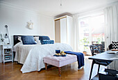 Double bed with pale bedspread and bench in bedroom