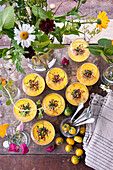 Tomatensuppe mit Topping serviert in Gläsern daneben ein sommerlicher Blumenstrauß
