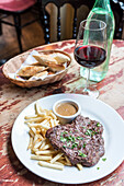 Traditionelles französisches Steak mit Pommes frites, Sauce und einem Glas Rotwein