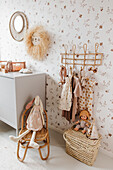 Girls' clothes on clothes pegs, toys and chest of drawers in nursery with patterned wallpaper
