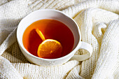 Cup of hot tea with lemon and white knitted sweater as a winter concept