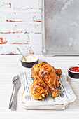 Roasted chicken legs drumsticks on wooden board with newspaper sheet served with ketchup and mayonnaise