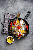 Roasted sea bream with lemon, herbs and tomatoes in cast iron skillet