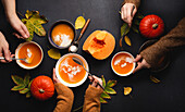 Pumpkin cream soup in plates on black background decorated with pumpkins and fall yellow leaves