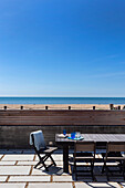 Tisch und Stühle auf der Terrasse mit Meerblick bei blauem Himmel