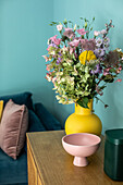 Lowboard with bouquet of flowers and bowl in front of blue wall