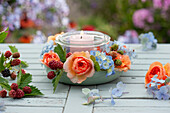 Dekoidee mit Kerze als Windlicht im Einmachglas, Blüten von Rosen und Hortensien mit unreifen Brombeeren als Kranz