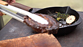 Grilled steak being removed from a pan