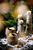 Glühwein in Keramikbechern mit Gewürzen, Orangen- und Apfelscheibe und Weihnachtsdeko