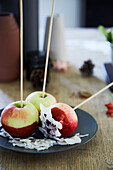 Candy apples on a stick with red sugar glaze and grated coconut on a plate