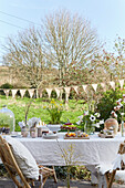 Table set for Easter meal outdoors with pale tablecloth below string of bunting