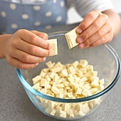 Breaking pieces of white chocolate into a bowl