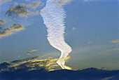 Long white contrail cloud snaking through dusk sky