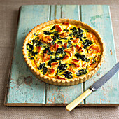 Salmon and spinach quiche on wooden board, knife nearby